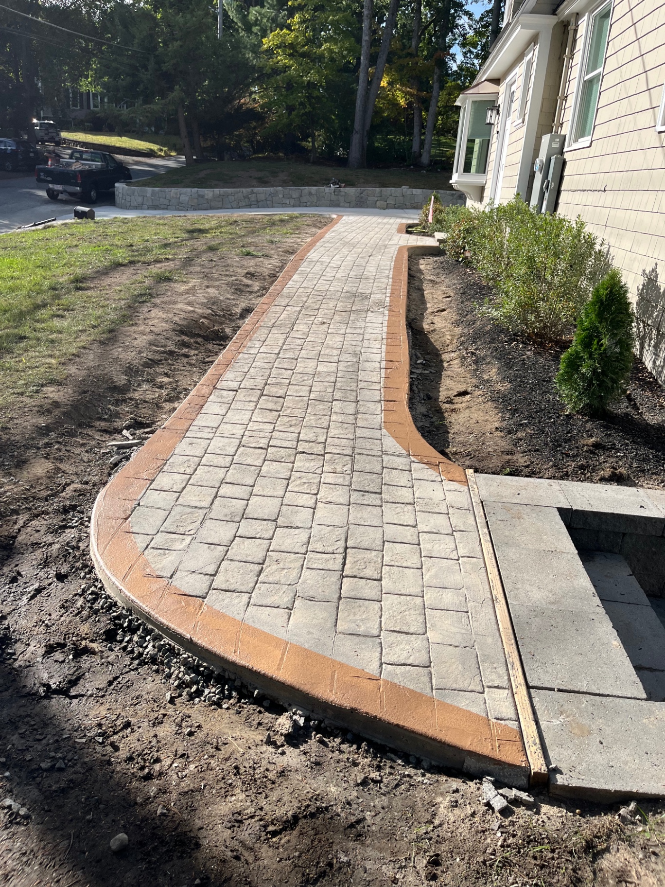 Curved stamped concrete walkway with colored border along a home